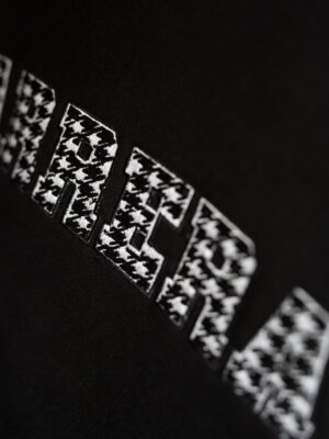 Close-up of black fabric featuring a row of white rectangular patches with a houndstooth-like pattern along a curved edge.