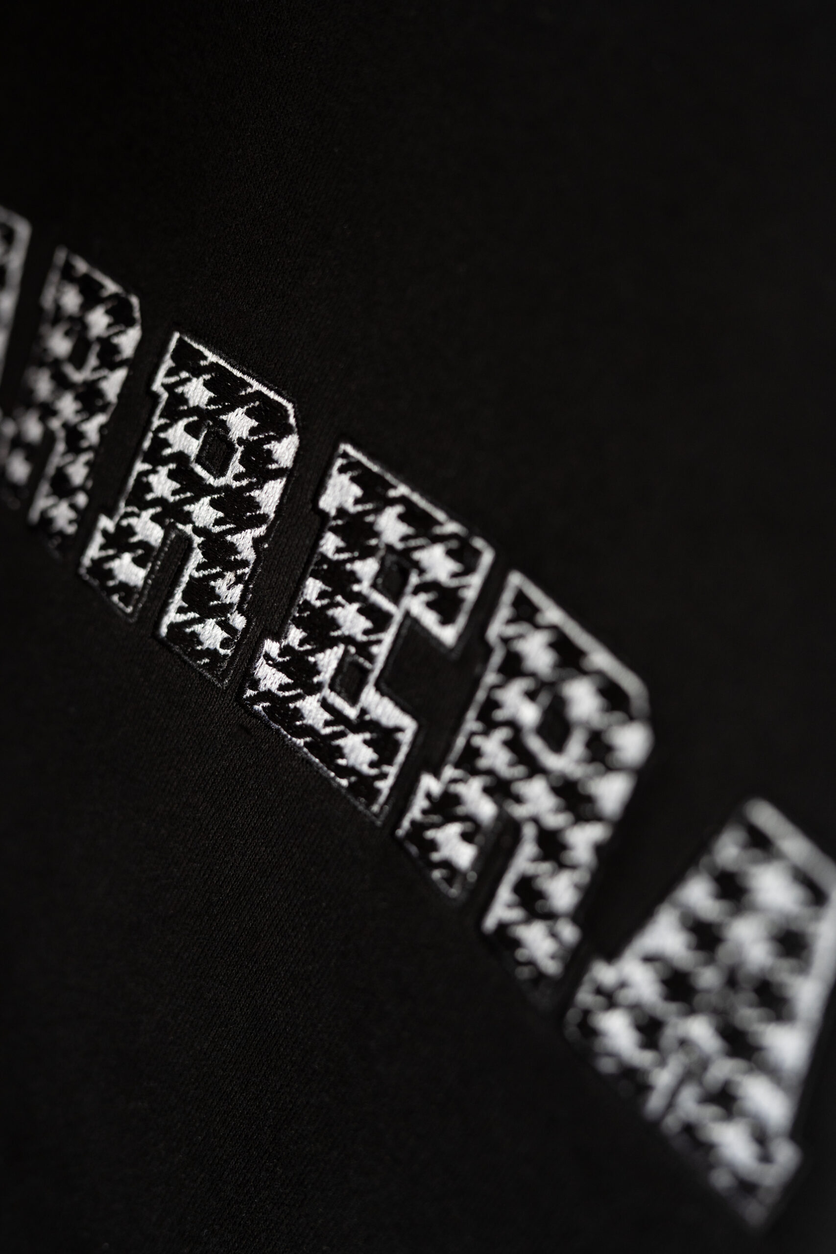 Close-up of black fabric featuring a row of white rectangular patches with a houndstooth-like pattern along a curved edge.